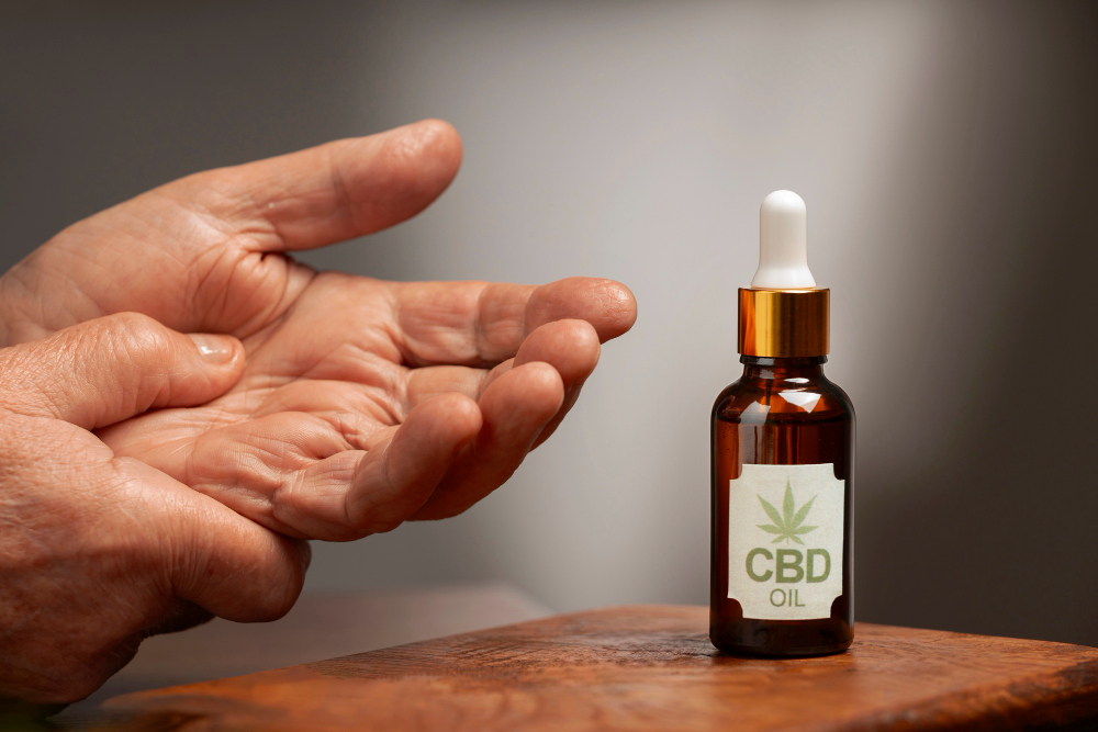 deux mains qui se massent avec un flacon d'huile de CBD placé à côté sur un morceau de bois, CBD 